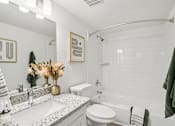 Thumbnail 9 of 34 - Studio Apartments in North Mountain Village, Phoenix, AZ - Ardella on 28th - Bathroom with Wood-Style Flooring, Granite Counter Sink with White Cabinetry, Mirror, and White Tile-Lined Shower with Tub.