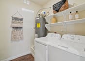 Thumbnail 14 of 39 - A laundry room with a washer and dryer, a basket on the shelf, and a wall hanging.