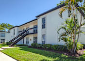 Thumbnail 34 of 34 - A white building with a black staircase and a palm tree in front.