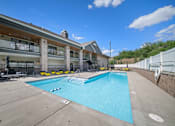 Thumbnail 3 of 47 - A large swimming pool in front of a building with a white fence on the right side.
