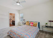 Thumbnail 11 of 39 - A bedroom with a bed, a fan, and a small table.