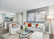 Thumbnail 8 of 34 - A living room with a grey sofa, a glass coffee table, and a large abstract painting on the wall.