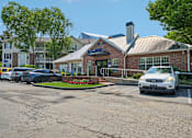 Thumbnail 30 of 34 - A white car is parked in front of a brick building with a blue sign.