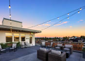 Thumbnail 33 of 50 - Apartments in Greenwood - The Morrow Rooftop Deck with Comfy Seating, Hanging Lights, Rectangular Fire Feature, and a Panoramic View of the City