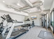 Thumbnail 12 of 34 - Studios in North Mountain Village, Phoenix, AZ - Ardella on 28th - Fitness Center With Treadmills, Cardio Equipment, Cable Machine, Mounted Monitor, Exposed Ductwork, and Large Windows.