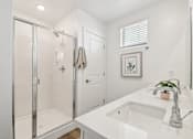 Thumbnail 24 of 45 - A white bathroom with a glass shower stall and a white sink.
