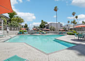 Thumbnail 14 of 34 - Phoenix Apartments - Ardella on 28th - Gated Outdoor Pool Area with Lounge Seating, Umbrellas, Tables with Chairs, and Surrounding Trees.