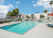 Thumbnail 15 of 34 - 1-Bedroom Apartments in North Mountain Village, Phoenix, AZ - Ardella on 28th - Resort-Style Swimming Pool With Sundeck, Lounge Chairs, Umbrellas, Trees, and Apartment Buildings Under Blue Sky.