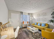 Thumbnail 8 of 46 - A living room with a yellow couch and a white chair.