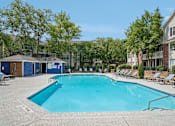 Thumbnail 23 of 34 - A large swimming pool surrounded by lounge chairs and trees.