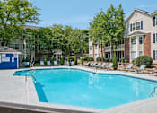 Thumbnail 24 of 34 - A swimming pool surrounded by lounge chairs and trees in front of apartment buildings.