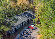 Thumbnail 18 of 25 - A parking lot with a building and cars is surrounded by trees.