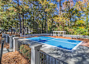 Thumbnail 2 of 25 - A blue pool surrounded by a fence and trees.