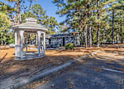 Thumbnail 22 of 25 - A gazebo sits in the middle of a paved area with trees in the background.