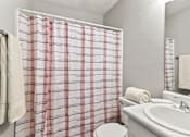 Thumbnail 16 of 25 - A white bathroom with a red and white checkered shower curtain.