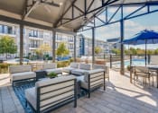 Thumbnail 22 of 40 - Apartments for Rent in Rowlett, TX - Village of Rowlett - Community Lounge Area Beside Swimming Pool and Grilling Stations with View of Apartment Buildings