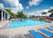Thumbnail 10 of 28 - A large outdoor swimming pool with blue lounge chairs and a white building with columns.