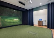 Thumbnail 13 of 28 - A room with a golf simulator and a green carpet.