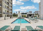 Thumbnail 11 of 31 - A large swimming pool surrounded by lounge chairs and apartment buildings.