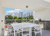 Thumbnail 16 of 31 - A white table and chairs are set up on a balcony with a cityscape in the background.