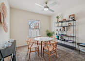 Thumbnail 9 of 39 - A room with a white table and chairs, a fan, and a shelf with various items.