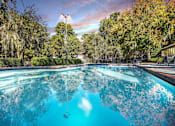 Thumbnail 2 of 16 - Greentree Apartments in Savannah, GA photo of a swimming pool with trees in the background and a cloudy sky