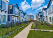Thumbnail 1 of 19 - Houses for Rent in Houston, TX - East Heights - Exterior View of Apartment Homes with Fences, Manicured Grass Yards, Concrete Walking Path, and Trees.