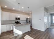Thumbnail 5 of 19 - Rental Homes in Houston, TX - East Heights - Kitchen with Vinyl Plank Flooring, White Cabinetry, Stainless Steel Appliances, Granite Countertops, Kitchen Island with Pendant Lights, and Tile Backsplash.