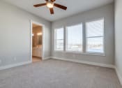 Thumbnail 10 of 19 - Luxury Three-Bedroom Homes for Rent in Houston, TX - East Heights - Carpeted Bedroom with Large Windows, Soft Grey Walls, Attached Bathroom, and Ceiling Fan.
