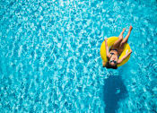 Thumbnail 8 of 15 - A woman in a yellow swim ring is floating in a pool.
