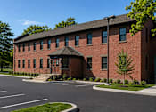 Thumbnail 18 of 25 - A red brick building with a black roof and a tree in front.