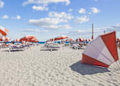 Thumbnail 5 of 9 - Modern Apartments in Downtown Miami 33139 for Rent – The Anamar at Collins Park – A beach scene with umbrellas and chairs.