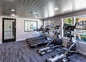 Thumbnail 4 of 28 - One Bedroom Apartments in Moreno Valley CA - Ardella on Chagall - Fitness Center with Cardio Equipment, Large Windows, and View of the Pool