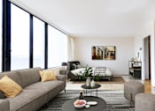 Thumbnail 9 of 66 - A living room with a grey couch, a coffee table, and a large window.