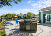 Thumbnail 9 of 29 - A sunny day at the poolside with a stone grill and chairs.