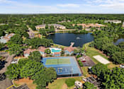 Thumbnail 2 of 29 - A tennis court is surrounded by trees and a lake.