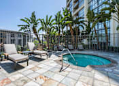 Thumbnail 18 of 29 - Pet-Friendly Apartments in Irvine, CA - Astoria at Central Park West - Spa with Lounge Seating, Surrounded by Grey Fencing, Potted Plants, and Tropical Trees.