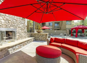Thumbnail 16 of 24 - 2-Bedroom Apartments in Sacramento, CA - Avanti - Outdoor Fireplace with Couch, Umbrella, and Cobblestone Bench