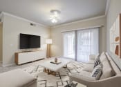 Thumbnail 3 of 24 - Sacramento, CA, Apartments Near Golden 1 Center - Avanti - Living Room with Plush Carpeting, Couch, Ottoman, Coffee Table, Media Console, TV, Ceiling Fan, and Sliding Glass Door with Access to Patio