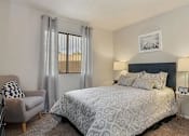 Thumbnail 13 of 46 - Apartments in Mesa, AZ - Mesa Station - Bedroom with Large Bed, Window with Curtains, Round Bedside Tables, ,Armchair and Carpeted Flooring.