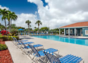 Thumbnail 9 of 28 - A poolside area with blue lounge chairs and a building in the background.