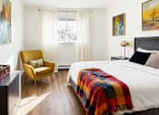 Thumbnail 7 of 35 - Twin Creek, Everett, WA, Apartments For Rent - Woodbrook - Bedroom With Vinyl Plank Flooring, Large Bed, Dresser, Armchair, Nightstand with Lamp, Insulated Windows, and Window Coverings.