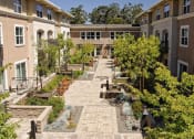 Thumbnail 8 of 11 - Dog-Friendly Apartments in Novato CA - Millworks - Courtyard Garden with Benches, Seating Area, Fountains, and Lush Greenery.