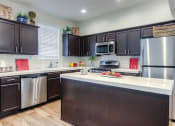 Thumbnail 1 of 14 - Tustin, CA Apartments for Rent - Tustin Cottages - Kitchen with an Island, Brown Cabinets, and Stainless-Steel Appliances