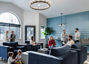Thumbnail 20 of 35 - A group of people are gathered in a room with blue couches and a chandelier.