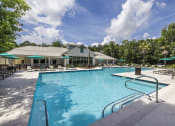 Thumbnail 2 of 35 - Savannah, GA Apartments – The Palms at Chatham– a large pool with lounge chairs and umbrellas in front of a building