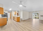Thumbnail 9 of 47 - A living room with a ceiling fan and light, hardwood floors, and a kitchenette with a sink and cabinets.