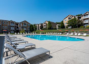 Thumbnail 15 of 31 - Pet-Friendly Apartments in Oak Ridge, TN – Centennial Village – a swimming pool with chaise lounge chairs in front of an apartment building
