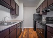 Thumbnail 24 of 28 - an empty kitchen with black appliances and wood flooring in an apartment