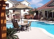 Thumbnail 9 of 13 - A pool with chairs and umbrellas in front of a house.